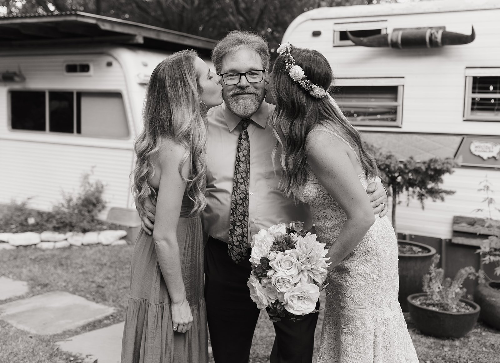 Black and white photo of Leah and her sister kissing their dad after the wedding