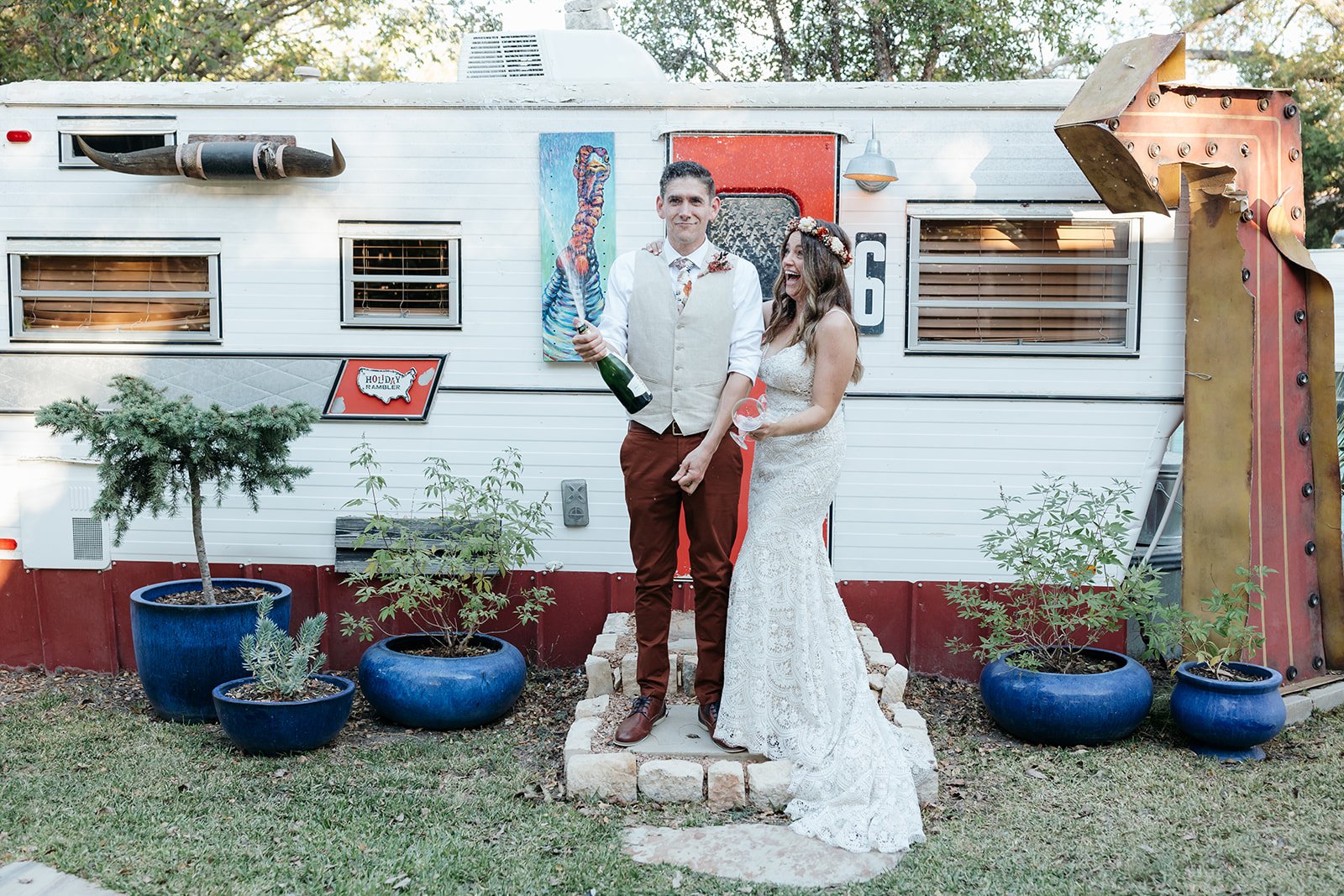 The couple popping champagne in front of the vintage remodeled camper trailers