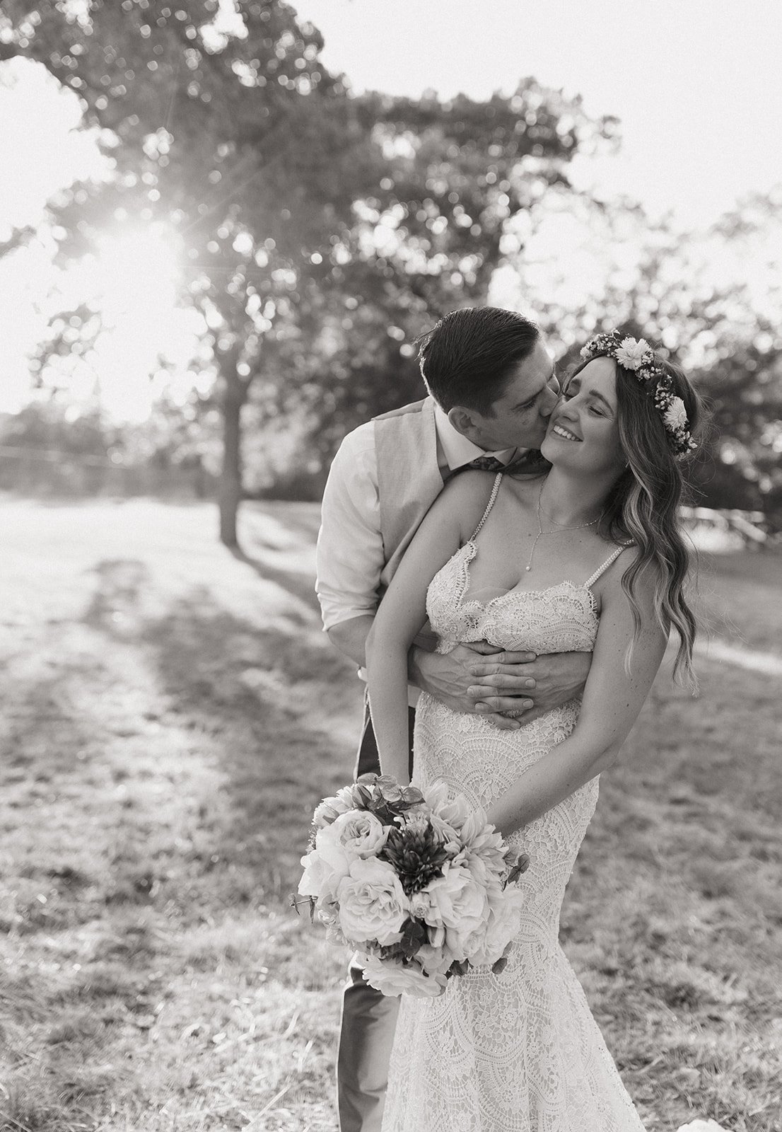 Emotive black and white photo of James kissing Leah on the cheek at golden hour 