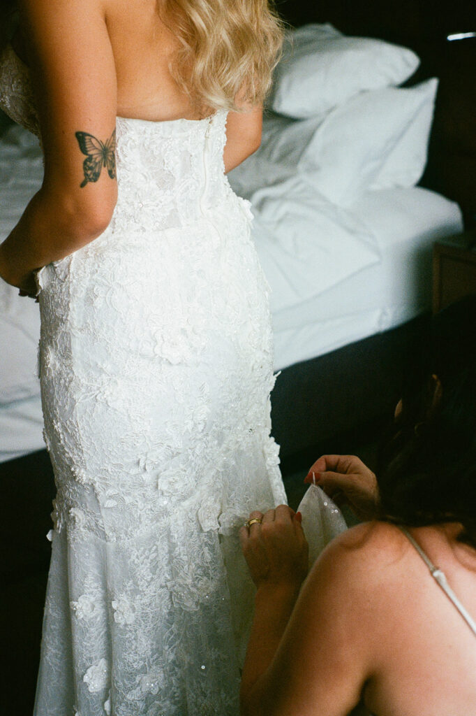 Bride getting her lace wedding dress adjusted by a bridesmaid