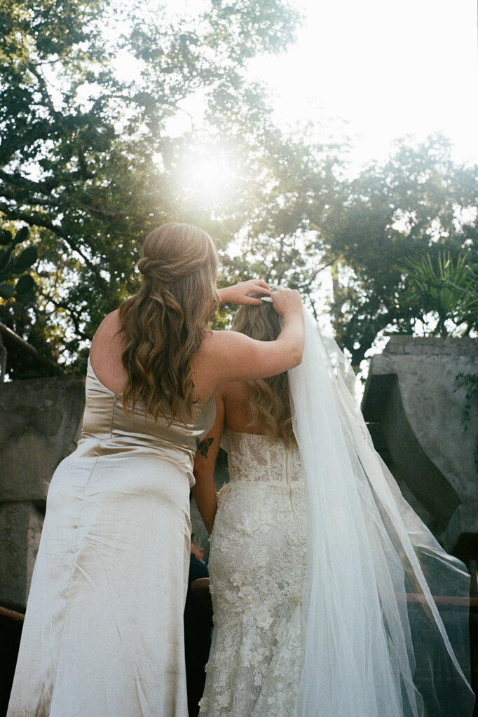 Bridesmaid adjusting the bride's veil in the sunlight at Villa Antonia, wedding photo shot on 35mm film