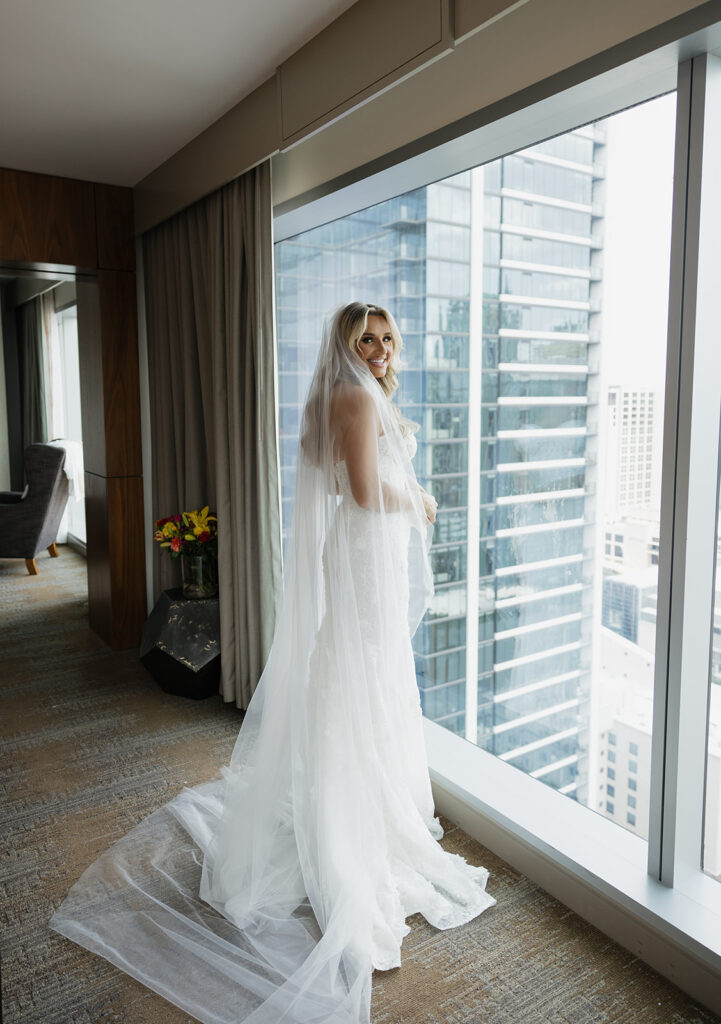 Bride in wedding dress by hotel window with Austin skyline, part of Austin TX wedding photos at JW Marriott Downtown Austin.