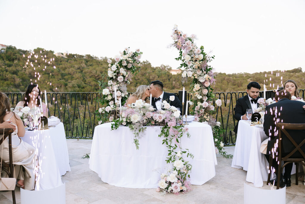 Bride and groom at sweetheart table with floral decor and sparklers at Villa Antonia wedding reception.