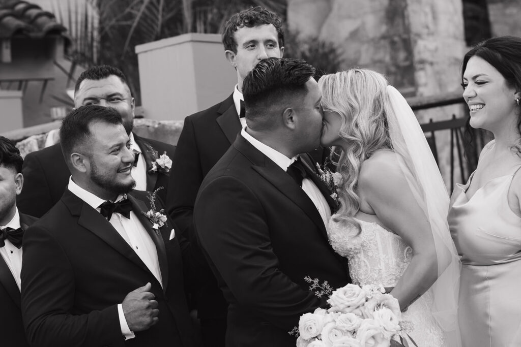 Bride and groom kiss surrounded by celebrating groomsmen and bridesmaids at Villa Antonia wedding reception