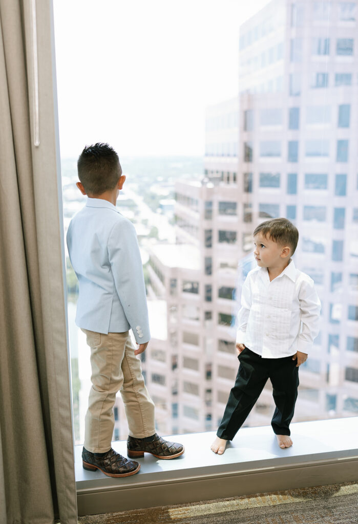 Young boys looking out of hotel window with city views, part of the groom's getting ready photos at the JW Marriott in downtown Austin