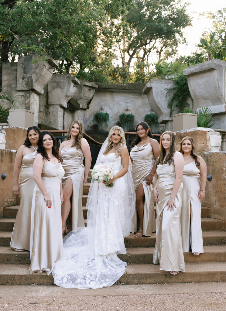 Bride with bridesmaids in satin dresses on stone steps at Villa Antonia wedding reception