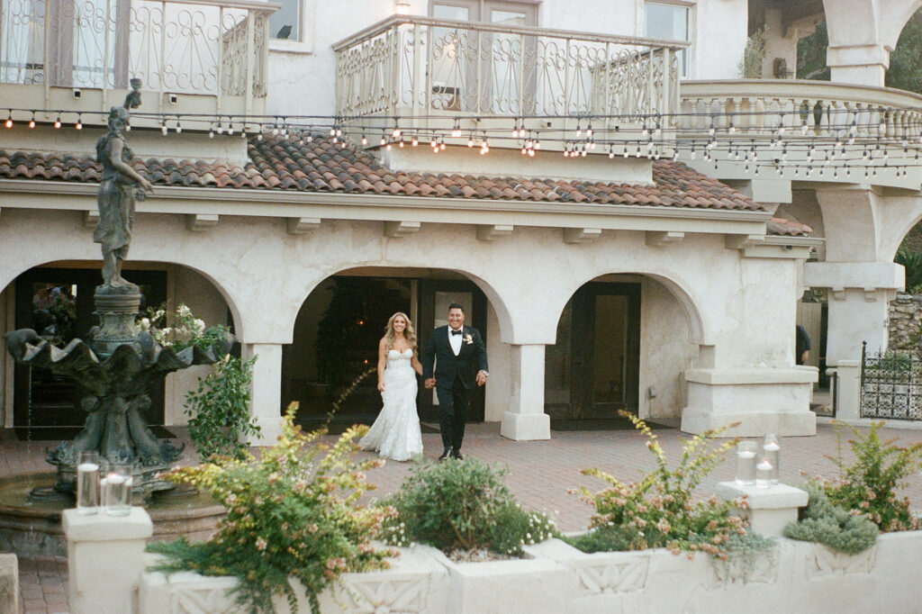 Bride and groom walking into Villa Antonia courtyard with greenery and stone arches, captured on 35mm film for their Villa Antonia wedding reception