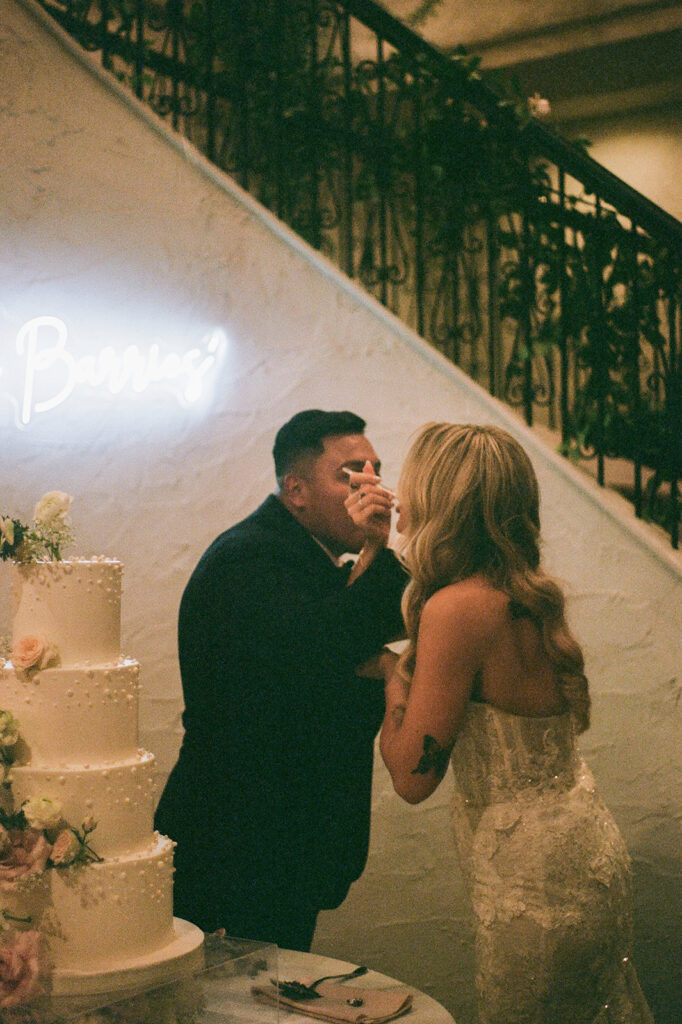 Bride and groom cutting wedding cake at villa Antonia wedding reception with neon sign in background, shot on 35mm film for a nostalgic feel