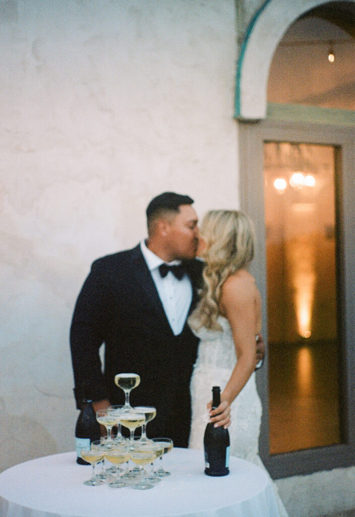 35mm film photo of bride and groom kissing by their champagne tower at their outdoor Villa Antonia wedding reception