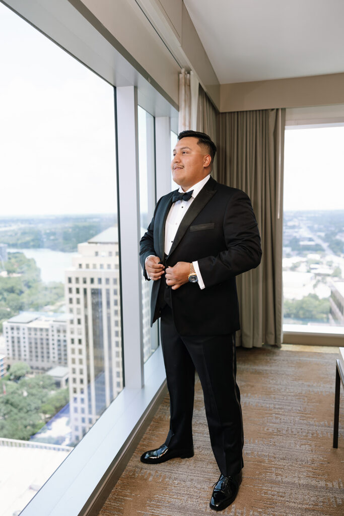 Groom adjusting tuxedo by window with city view for Austin TX wedding photos at JW Marriott.