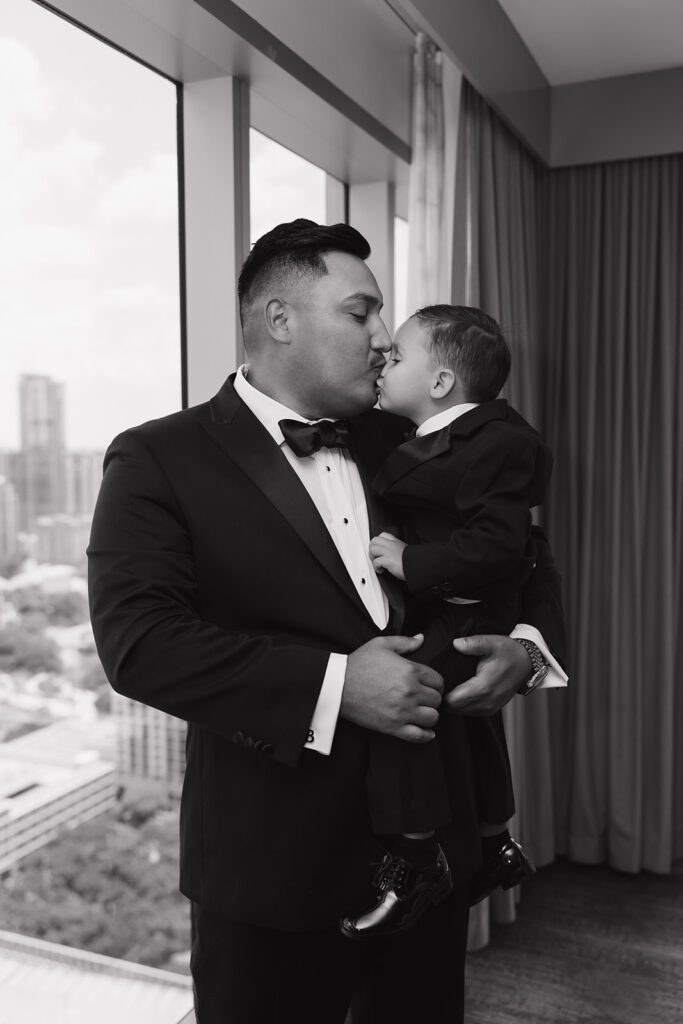 Groom sharing a sweet kiss with toddler son in front of his getting ready suite at the JW Marriott