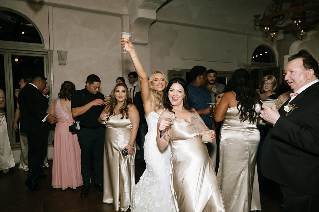 Bride raising a glass and dancing joyfully with one of her bridesmaid's on the Villa Antonia dance floor 