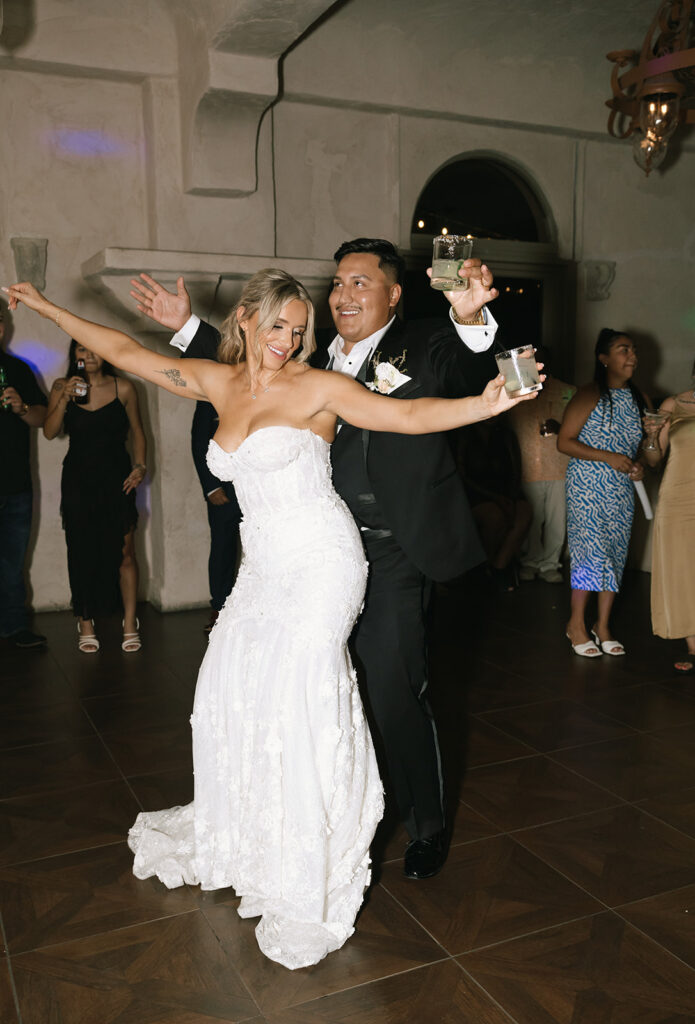 Bride and groom getting down on the dance floor together with cocktails in hand