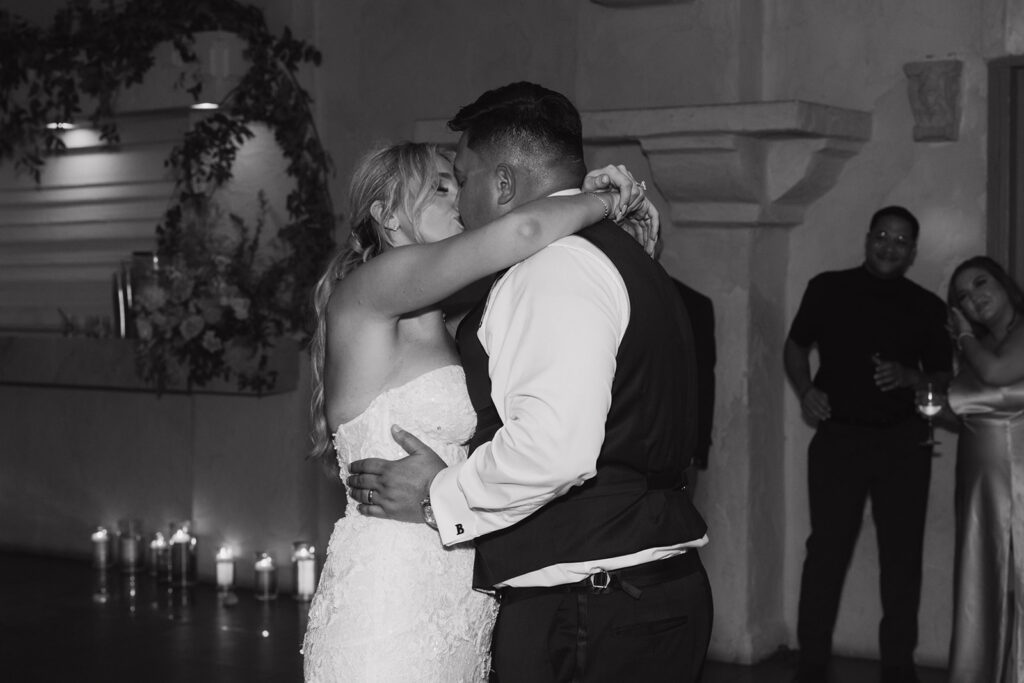 Bride and groom sneaking a kiss on the dance floor with friends and family around