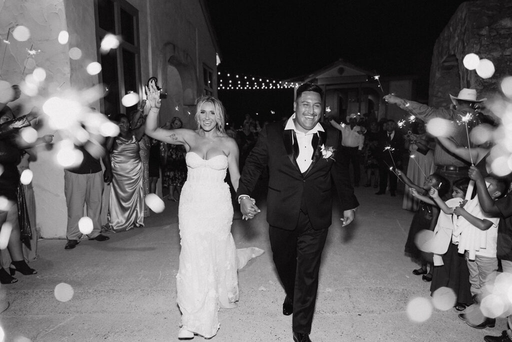 Bride and groom holding hands and smiling as they exit Villa Antonia, surrounded by sparklers 