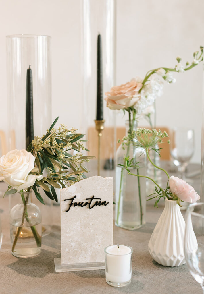 Table number fourteen styled with soft blush blooms, black taper candles, and clear vases.