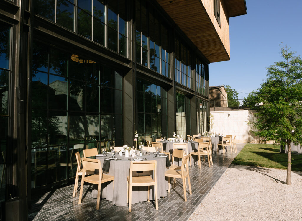 Outdoor wedding reception setup at Albert Hotel Fredericksburg with natural wood chairs and modern black-framed windows in the background.