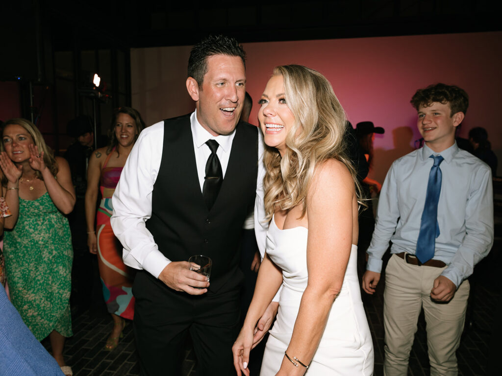 The newlyweds celebrating on the dance floor, smiling and surrounded by guests.