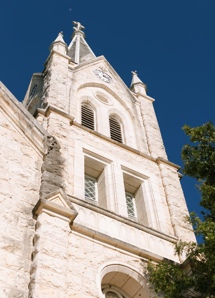 Exterior stone bell tower of St. Mary’s Catholic Church in Fredericksburg, Texas, captured against a clear blue sky.