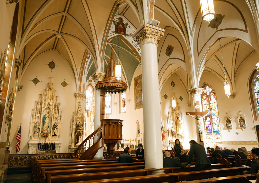 Interior view of the cathedral-style sanctuary at St. Mary’s, with guests seated and warm light filtering through the stained glass windows.