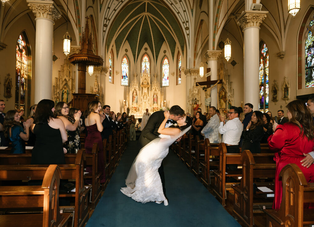 Candid moment of Shannon and Austin kissing at the end of the aisle with golden light streaming in from the windows right after the ceremony at St. Mary’s in Fredericksburg.