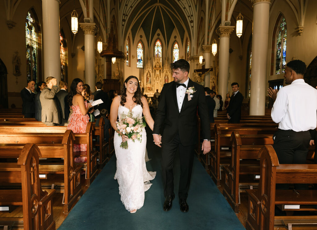 Shannon and Austin walking up the aisle together after saying “I do” at St. Mary’s Catholic Church, beaming as newlyweds.