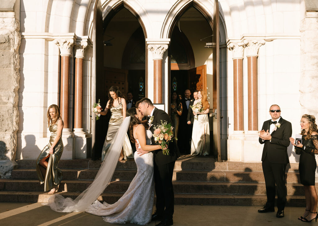 Romantic portrait of Shannon and Austin kissing outside the entrance of St. Mary’s, sunlight glowing through her veil as guests cheer nearby.