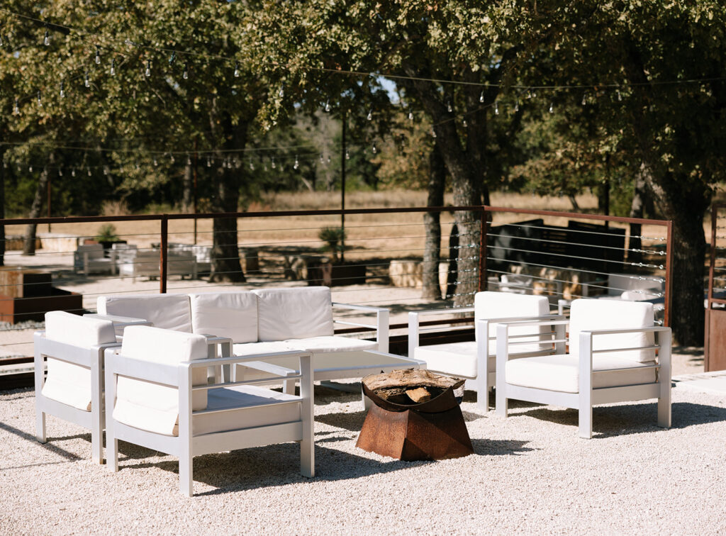Outdoor lounge area in the Fireside Courtyard at Swallows Eve, with white modern seating and a fire pit—perfect for cocktail hour mingling under the trees.