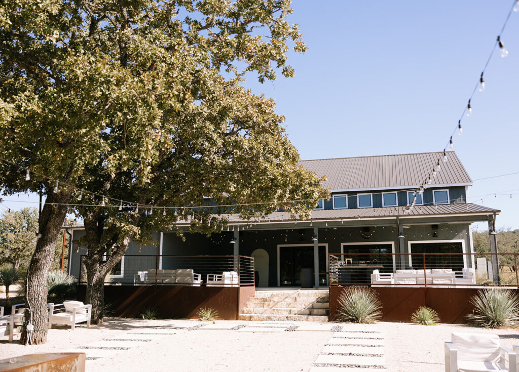 View of the back of the barn at Swallows Eve with open-air stairs leading down to the Fireside Courtyard, surrounded by large oak trees and soft natural light.