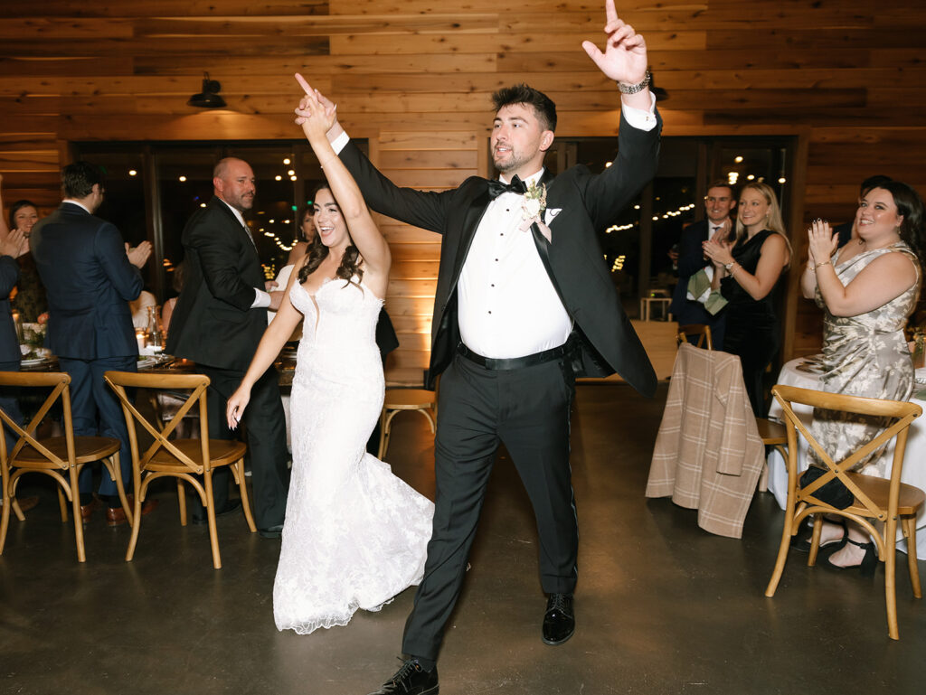 Shannon and Austin dancing during their grand entrance at Swallows Eve indoor reception barn, surrounded by guests and big cutouts of their dog’s face.
