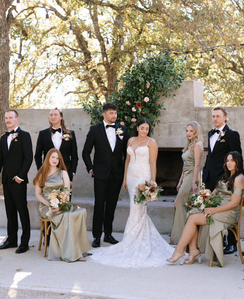 Wedding party seated and standing in the courtyard at Swallows Eve, dressed in elegant black and champagne tones, posed in soft natural light.