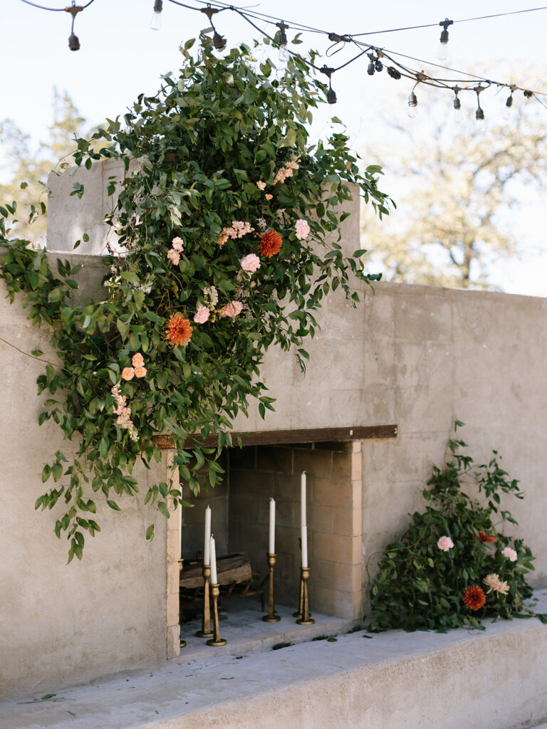 Ceremony florals and entrance setup in the Fireside Courtyard at Swallows Eve, featuring greenery and blush-toned blooms against the stone fireplace backdrop.