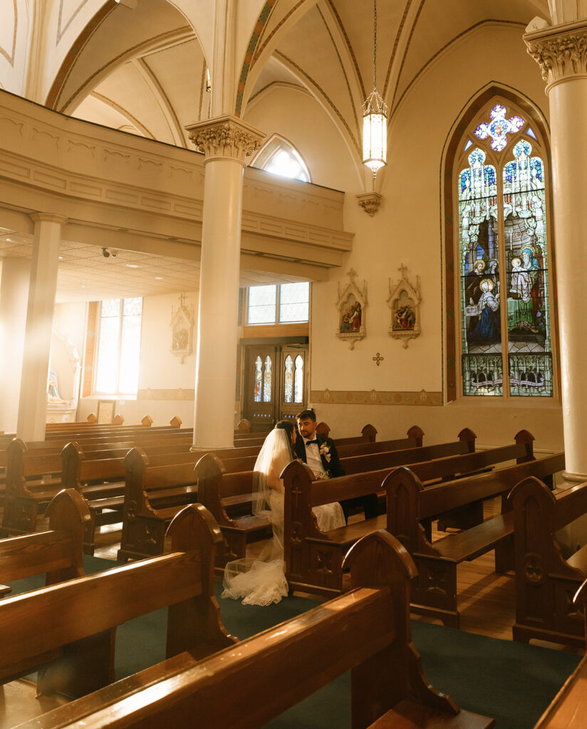 Shannon and Austin sharing an intimate moment sitting in the pews at St. Mary’s Catholic Church in Fredericksburg, with golden hour light glowing through the stained glass windows.