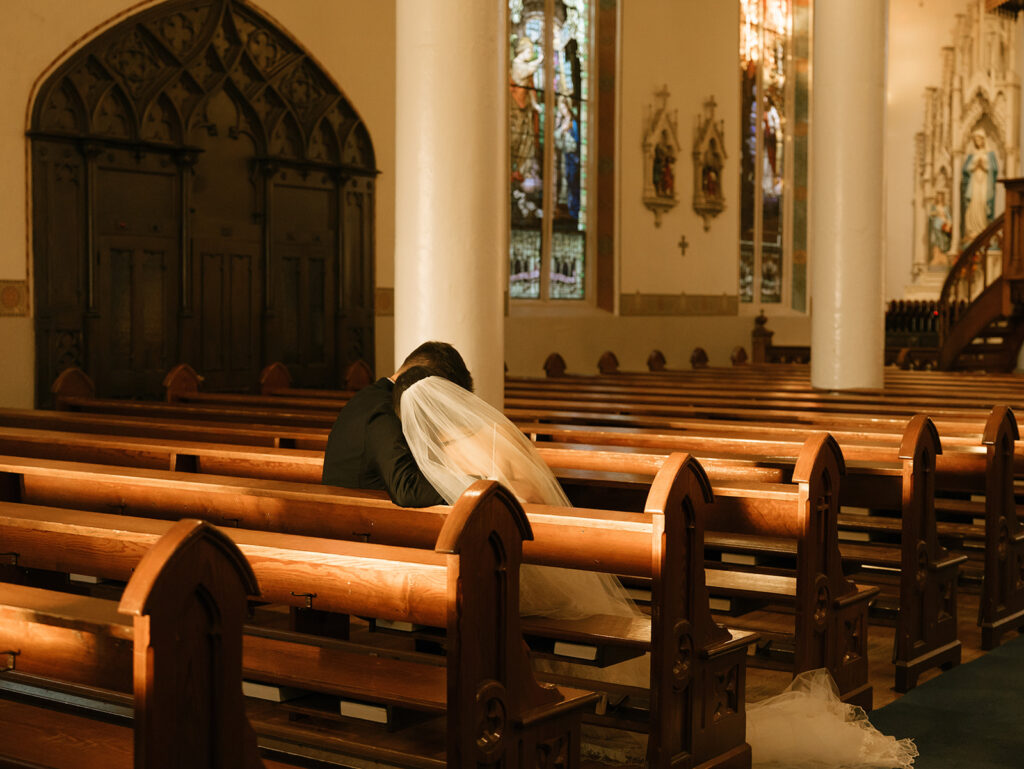 Shannon resting her head on Austin’s shoulder during golden hour portraits inside St. Mary’s Catholic Church, bouquet in hand and veil draped softly.