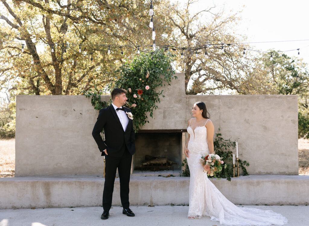 Shannon and Austin smiling at each other during their Fredericksburg Texas wedding first look, framed by soft sunlight and romantic greenery.
