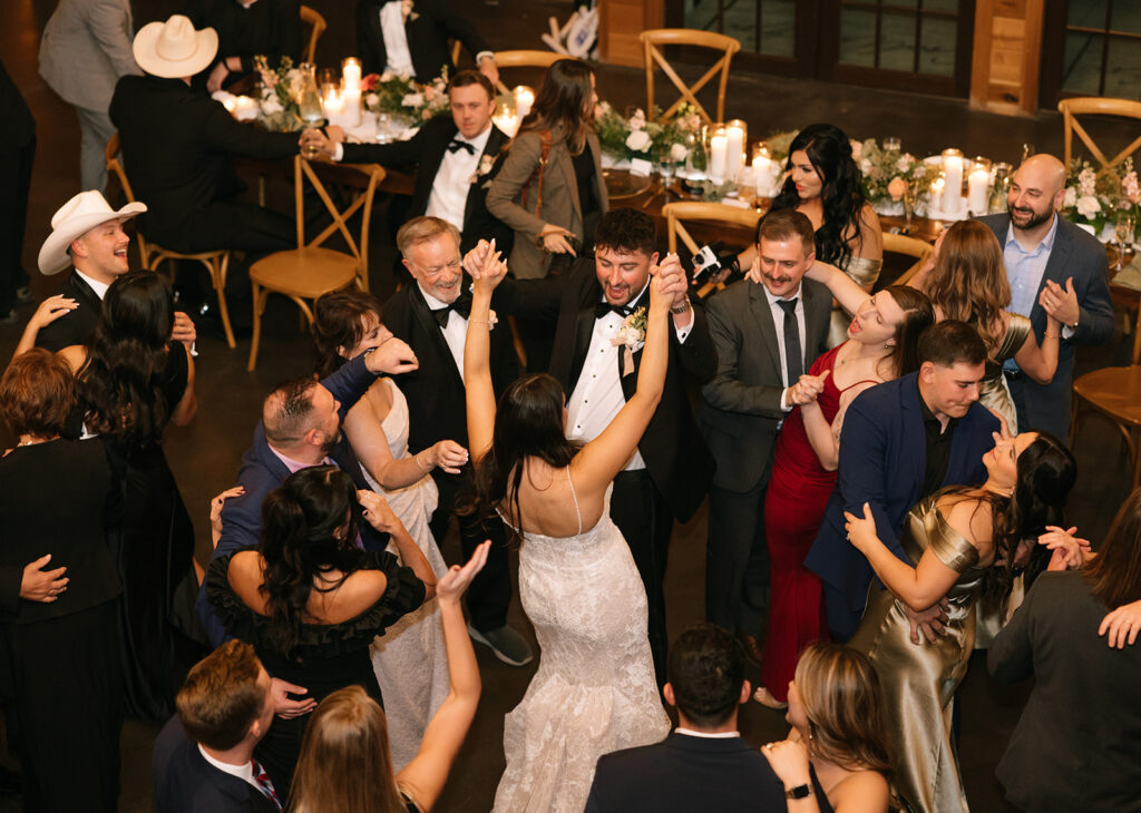 Group of wedding guests cheering and dancing with Shannon and Austin on the Swallows Eve reception dance floor, kicking off the evening celebration.
