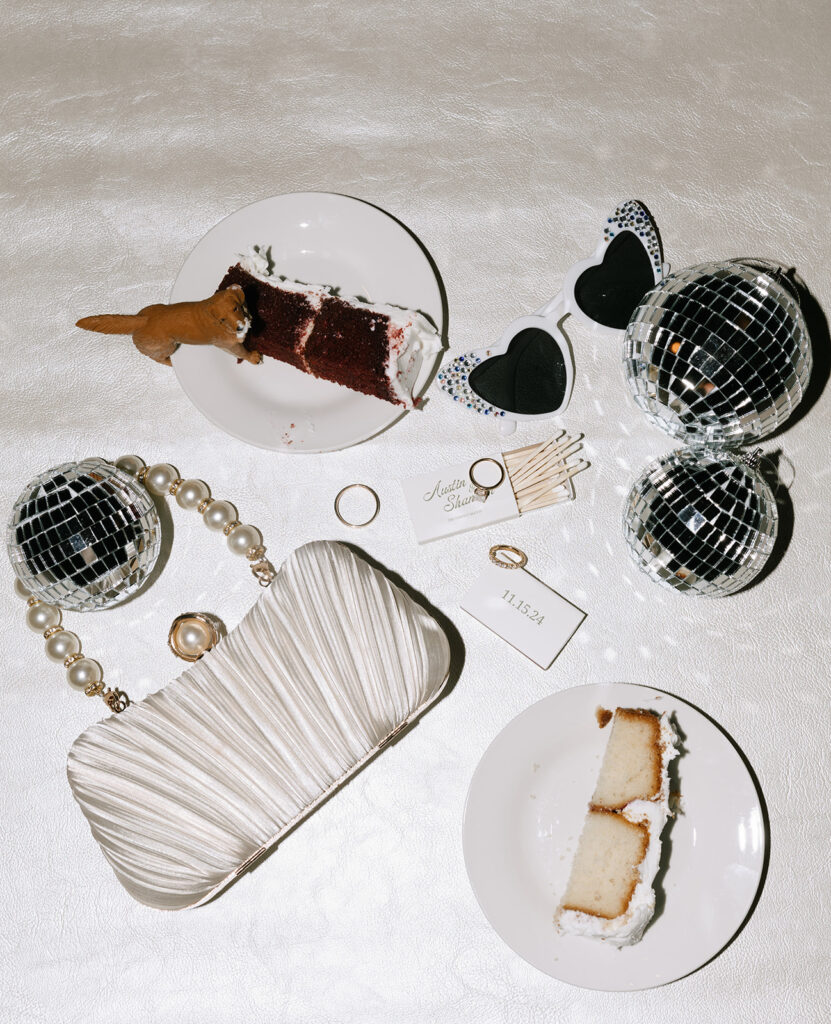 Flash flatlay of Shannon’s bridal clutch, wedding rings, matchbook favors, and disco balls—styled with cake slices and heart sunglasses for a playful, late-night reception look.