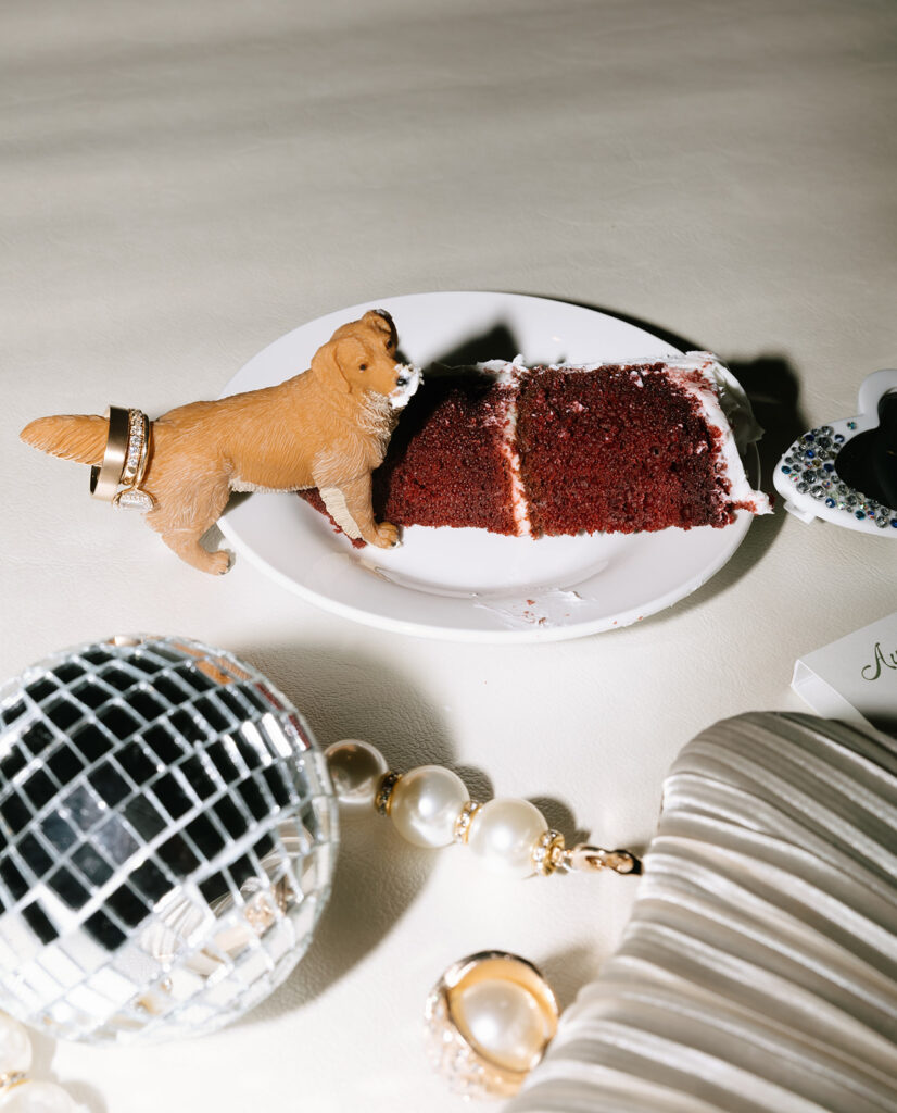Close-up flatlay of cake slice with a dog figurine “sneaking a bite,” surrounded by disco balls and bridal accessories at this Fredericksburg Texas wedding.