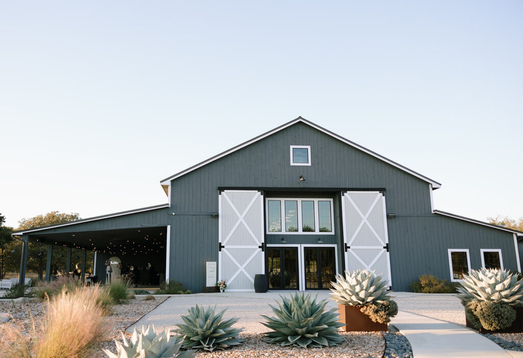 Exterior view of the barn at Swallows Eve in Fredericksburg Texas, a refined Hill Country wedding venue surrounded by agave plants and oak trees.