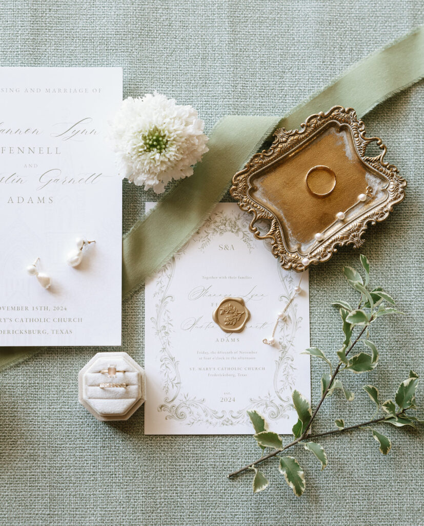 Flatlay of Shannon’s wedding details at Swallows Eve featuring her invitation suite, heirloom gold ring tray, floral accents, and velvet vow booklet.