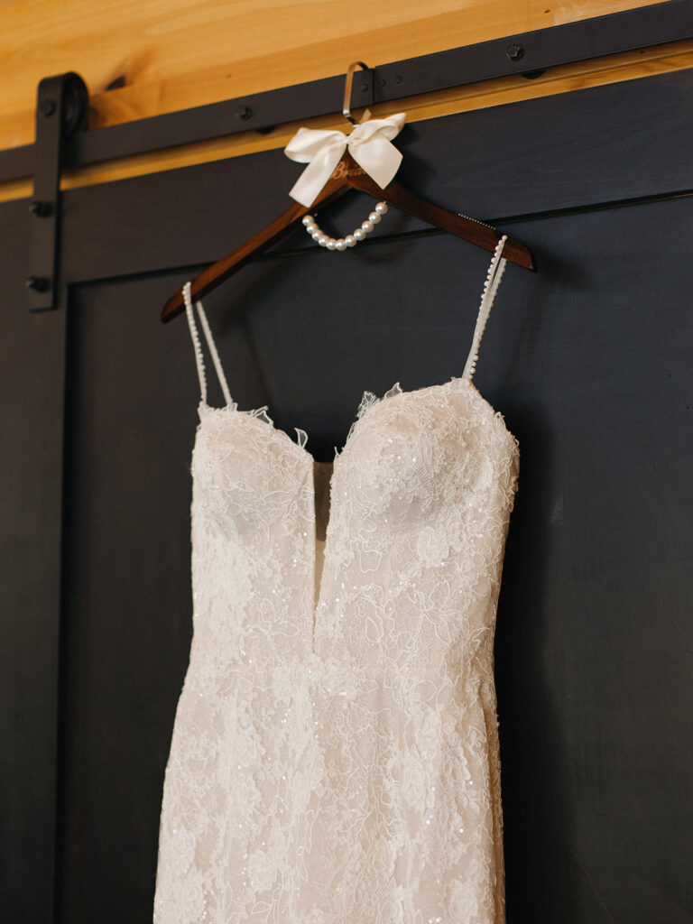 Full view of Shannon’s elegant lace wedding gown with sweetheart neckline hanging on a black barn door inside the Swallows Eve bridal suite.