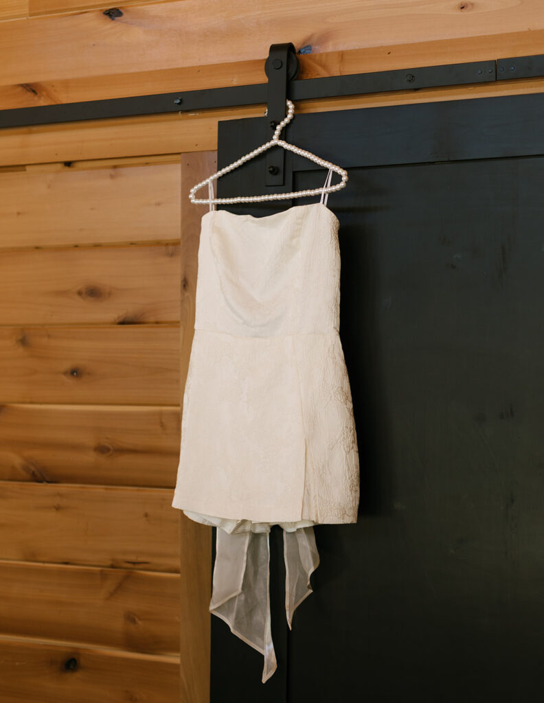 Minimal ivory reception dress hanging beside wood-paneled walls—Shannon’s chic second look for her Fredericksburg Texas wedding celebration.