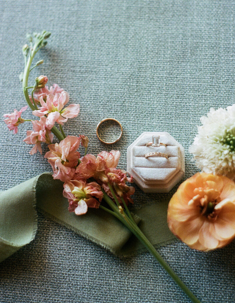 Flatlay of Shannon and Austin’s wedding rings, soft peach florals, and velvet ring box—captured on 35mm film for a timeless detail moment.