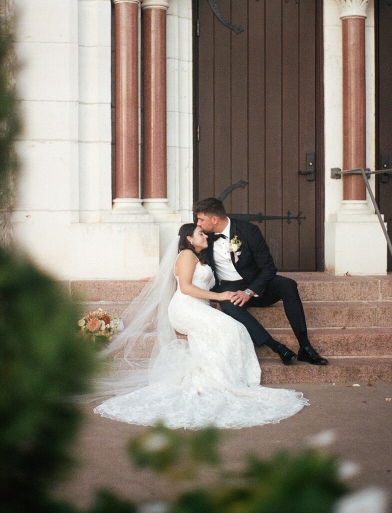 Shannon and Austin sitting on the steps outside St. Mary’s Catholic Church in Fredericksburg, sharing a quiet post-ceremony moment on 35mm film.