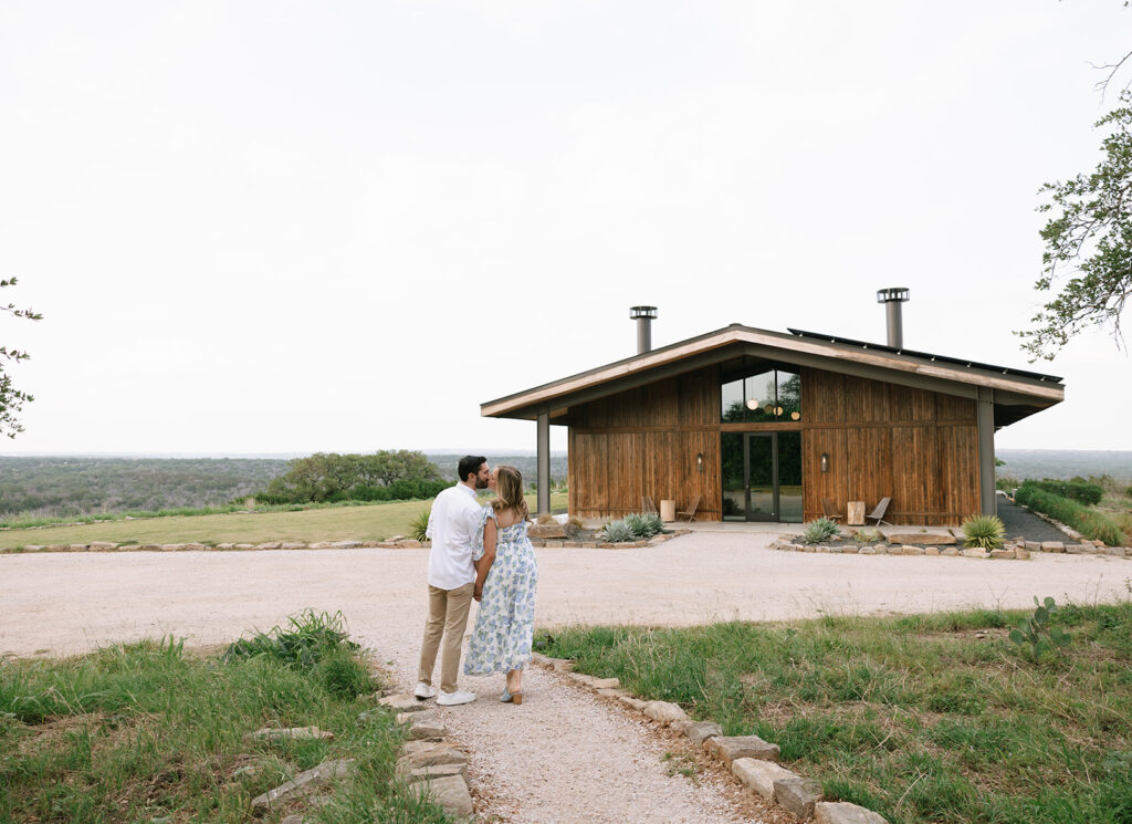 Sara and Kyle walking hand-in-hand toward the Walden Retreats event space, surrounded by Hill Country views.