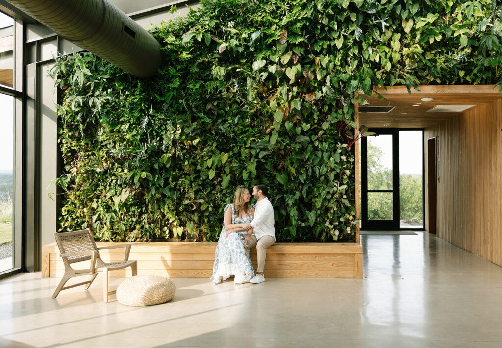 Engagement photo of the couple sitting beneath the iconic greenery wall inside the Walden Retreats event space.