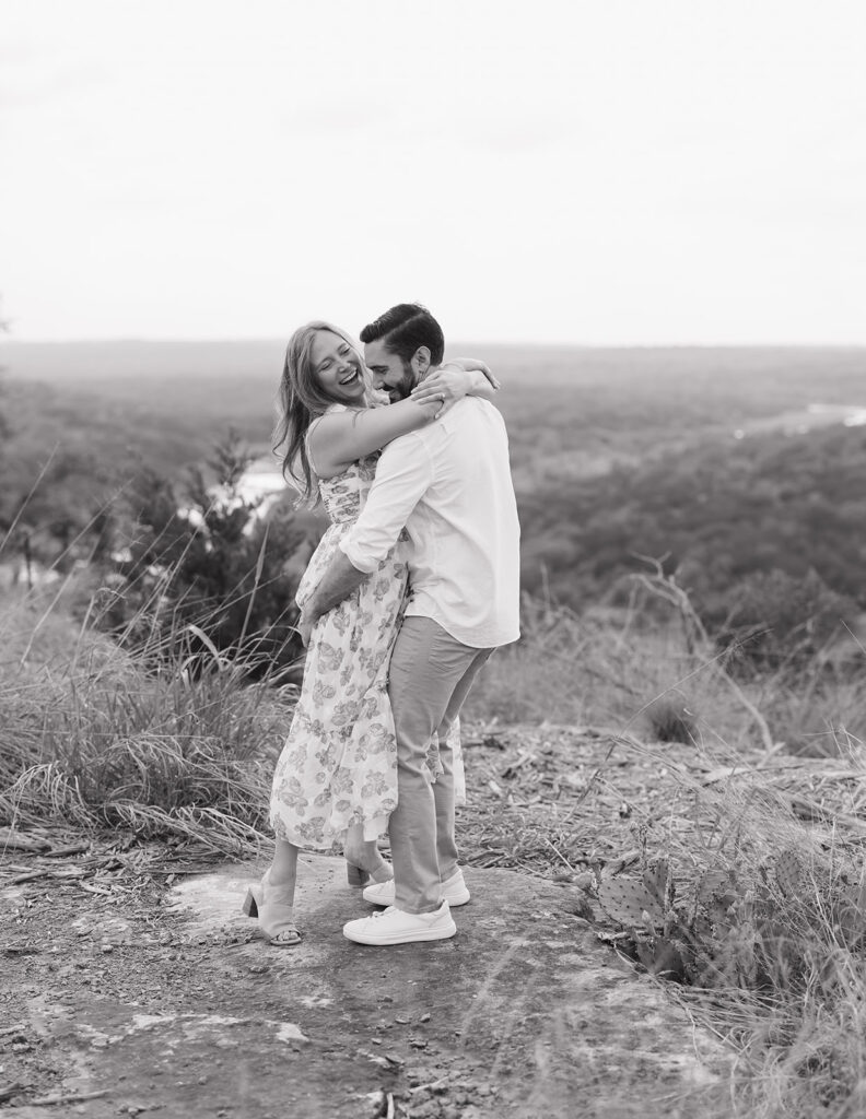 Black and white photo of the couple laughing and embracing with sweeping Hill Country views behind them at Walden Retreats.