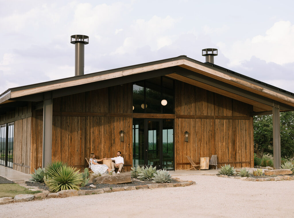 Couple sitting on the bench outside the modern event pavilion at Walden Retreats in Johnson City, surrounded by native plants and natural wood architecture.