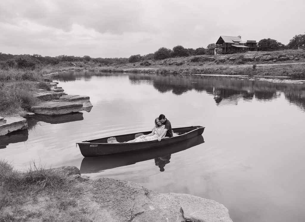 Wide black and white photo of the couple floating in a canoe on the Pedernales River with Walden Retreats visible in the distance.