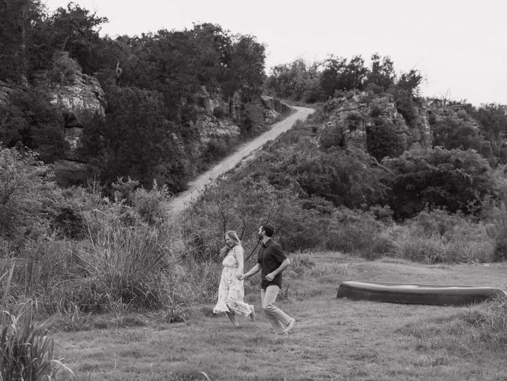 The couple laughing and running hand-in-hand near the canoe launch point at Walden Retreats, surrounded by natural Hill Country cliffs and trails.
